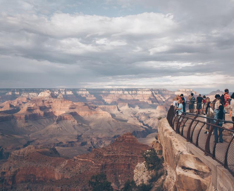 A group of people standing at a railing at the top of a cliff looking at a vista of the Grand Canyon