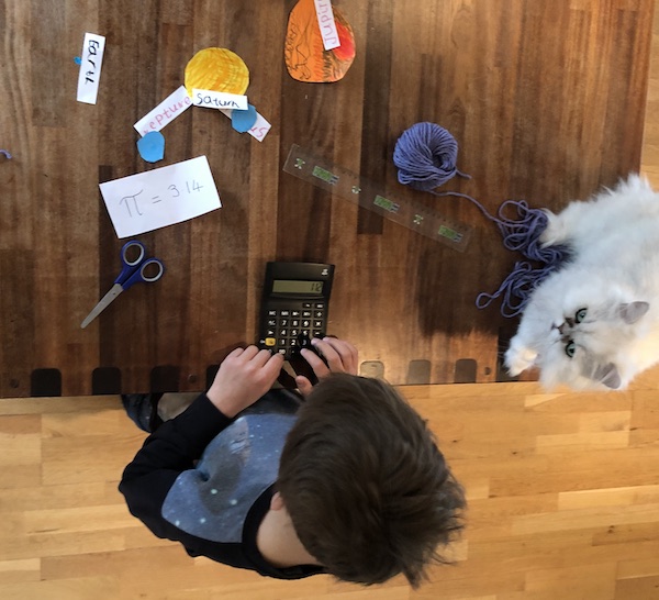 Child computing the circumference of scale models of planets using fruit